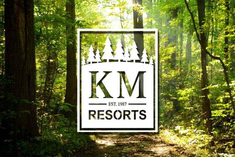 K/M Resorts of America Campground Membership Resales A premium travel trailer RV camper parked on a spacious campsite next to a calm lake at a K/M Resorts of America private campground preserve in the Pacific Northwest.
